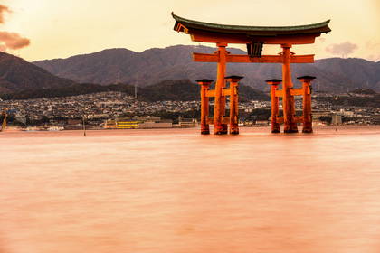 Pomarańczowa brama torii Itsukushima na wodzie, w tle góry.