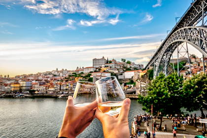 Dwie osoby wznoszą toast kieliszkami wina na tle miasta Porto i mostu Ludwika I.