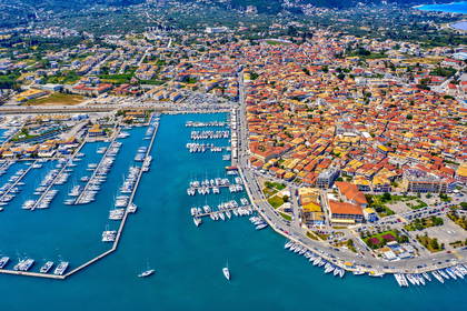 Widok z lotu ptaka na port w Lefkadzie, Grecja. W porcie zacumowane jachty, w tle miasto z czerwonymi dachami.