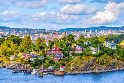 Oslo widziane od strony morza. Na pierwszym planie kolorowe domy na wzgórzu, w tle ratusz.