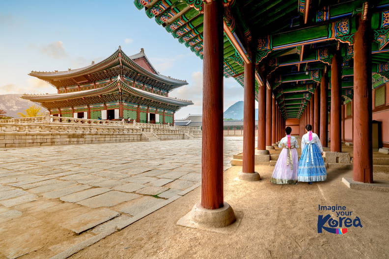 Dwie kobiety w strojach hanbok spacerują korytarzem z widokiem na dziedziniec w pałacu Gyeongbokgung w Seulu.