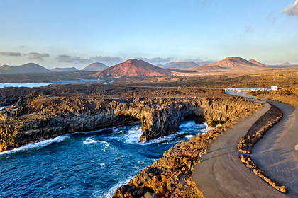 Skaliste wybrzeże Lanzarote z tunelami. W tle widoczne góry i droga.