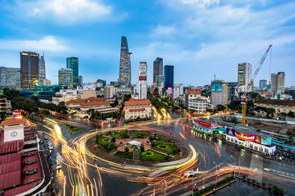 Panorama Ho Chi Minh nocą. Na pierwszym planie rondo z rozmazanymi światłami samochodów.
