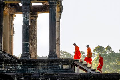 Trzech mnichów w pomarańczowych szatach schodzi po schodach w Angkor Wat.