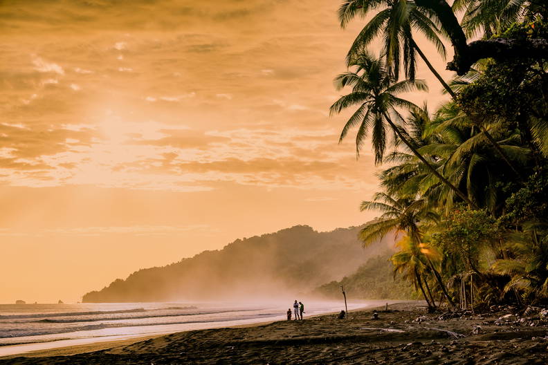 Zachód słońca na plaży. Widoczne palmy i sylwetki ludzi.