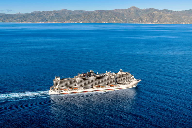 Biały statek wycieczkowy płynie po morzu. W tle widać góry.