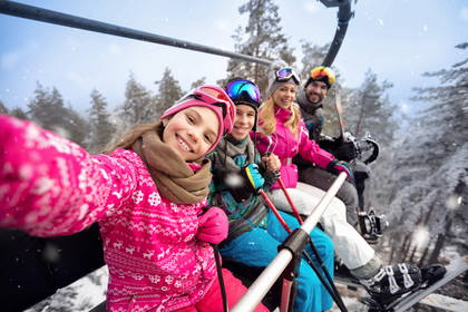 Uśmiechnięta rodzina robi sobie selfie na wyciągu narciarskim.