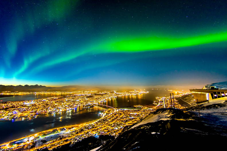 Widok z góry na zieloną zorzę polarną nad nocną panoramą Tromsø w Norwegii.