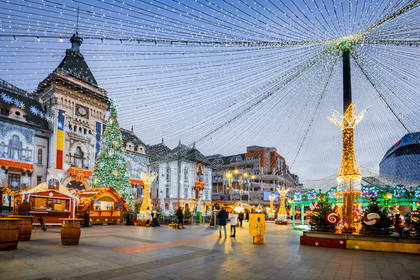 Jarmark świąteczny na placu Unirii w Jassach. Nad placem wisi świetlny dach z girland, a tło tworzą zdobione kamienice.