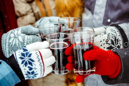 Zbliżenie na dłonie w zimowych rękawiczkach wznoszące toast grzanym winem.