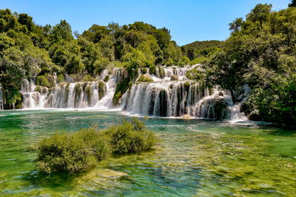 Park Narodowy Krka w Chorwacji. Szeroki wodospad z licznymi kaskadami wpada do szmaragdowego jeziora.