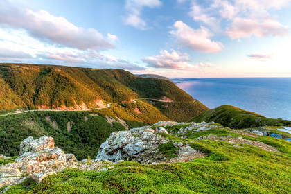 Kręta droga Cabot Trail na zboczu zielonych wzgórz nad oceanem o zachodzie słońca.