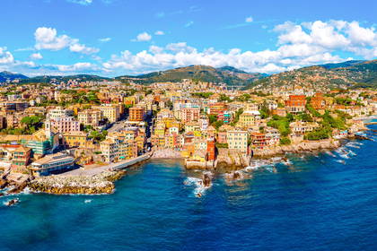 Panorama Boccadasse w Genui. Kolorowe kamienice stoją nad błękitnym morzem i skalistym wybrzeżem.