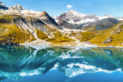 Ośnieżone szczyty gór w Parku Narodowym Glacier Bay na Alasce odbijają się w spokojnej tafli błękitnego jeziora.