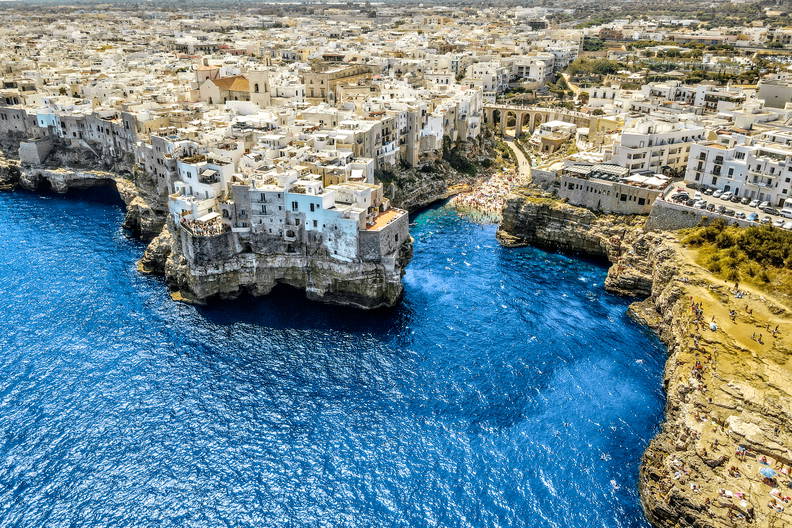 Widok z lotu ptaka na Polignano a Mare. Białe miasto na klifach nad błękitnym morzem, z plażą w małej zatoce.