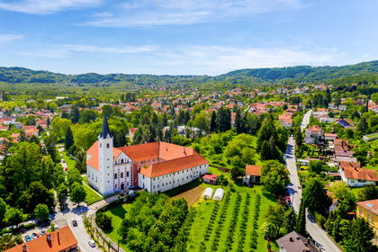 Widok z góry na Klasztor Franciszkanów w Samoborze. Biały kościół i miasteczko są otoczone zielonymi wzgórzami.