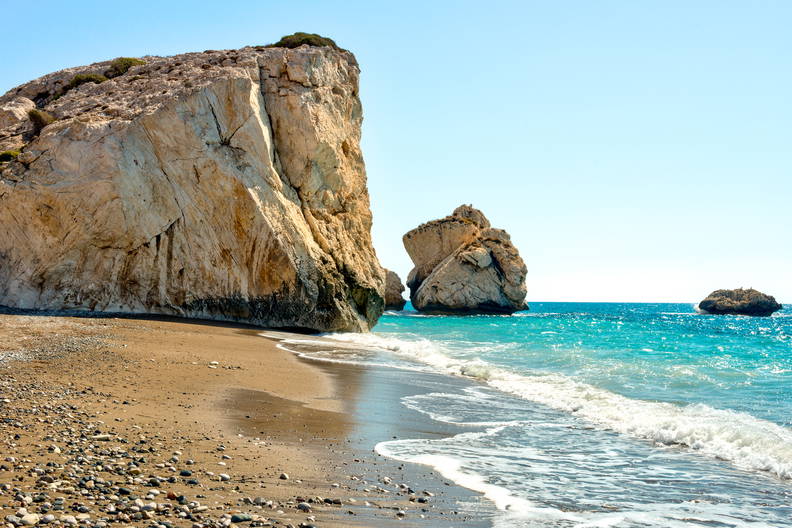 Petra tou Romiou, znana jako Skała Afrodyty na Cyprze. Kamienista plaża z dużymi formacjami skalnymi i turkusowe morze w słoneczny dzień.