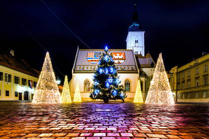 Kościół św. Marka w Zagrzebiu nocą, a na placu oświetlona choinka i świąteczne dekoracje.